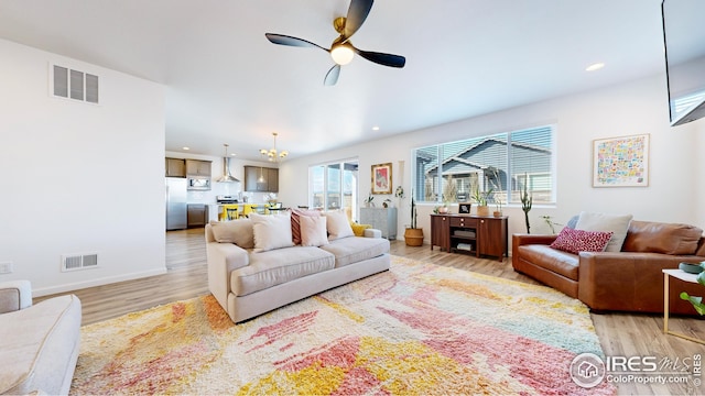 living room with light wood-style flooring, ceiling fan with notable chandelier, and visible vents