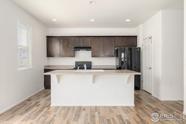 kitchen with a kitchen island with sink, dark brown cabinets, light hardwood / wood-style floors, and a breakfast bar