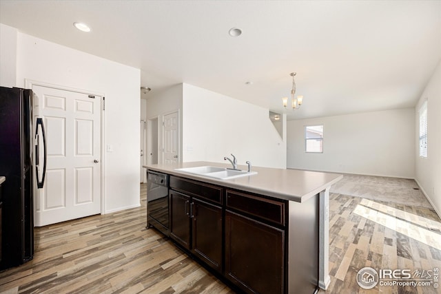 kitchen featuring sink, black appliances, a center island with sink, decorative light fixtures, and light wood-type flooring