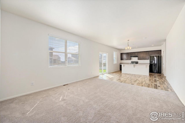 unfurnished living room featuring light carpet and a chandelier