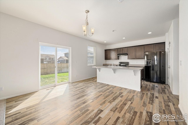 kitchen with a breakfast bar, electric range, dark brown cabinetry, black fridge with ice dispenser, and decorative light fixtures