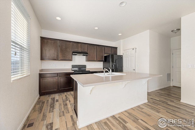 kitchen with dark brown cabinetry, sink, a kitchen island with sink, and black appliances