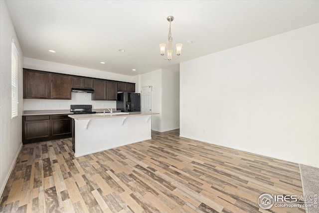 kitchen featuring dark brown cabinets, light wood-type flooring, a center island with sink, pendant lighting, and black appliances