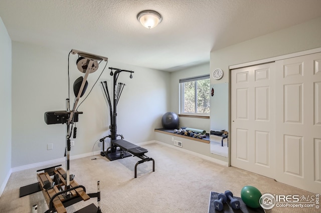 exercise room with light colored carpet and a textured ceiling