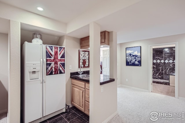 kitchen with light brown cabinetry, white refrigerator with ice dispenser, and dark colored carpet
