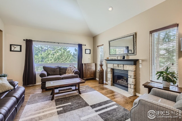 living room featuring a stone fireplace, vaulted ceiling, and light hardwood / wood-style floors