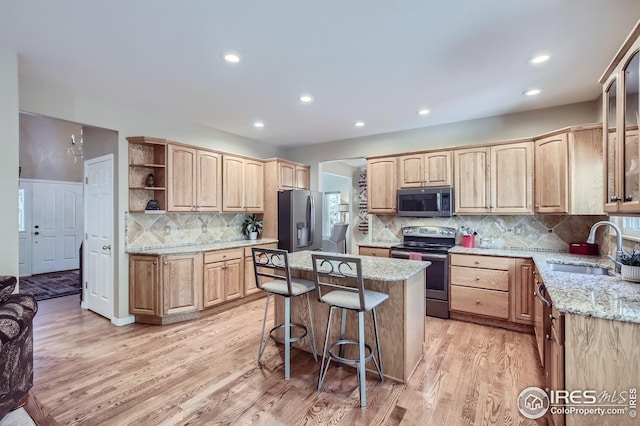 kitchen featuring sink, light stone counters, a center island, appliances with stainless steel finishes, and light hardwood / wood-style floors