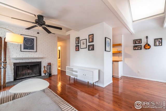 living room featuring wood-type flooring, a brick fireplace, ceiling fan, and beam ceiling