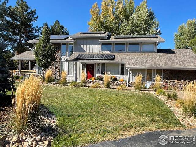 view of front of home featuring a front yard, a shingled roof, and roof mounted solar panels