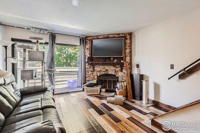 living room with a stone fireplace, baseboards, and wood finished floors