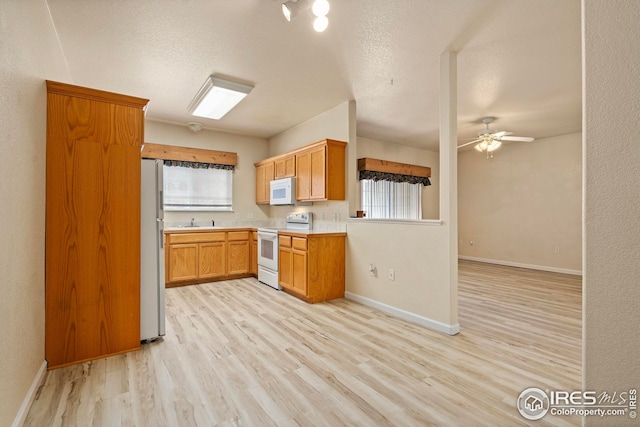 kitchen featuring sink, white appliances, ceiling fan, a textured ceiling, and light wood-type flooring