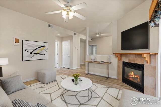 living room featuring ceiling fan, a tiled fireplace, and light hardwood / wood-style flooring