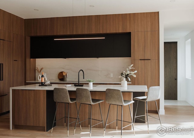 kitchen featuring sink, a breakfast bar, a kitchen island with sink, decorative light fixtures, and light wood-type flooring