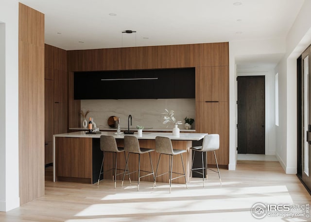 kitchen with a kitchen bar, sink, light hardwood / wood-style flooring, a large island with sink, and decorative backsplash