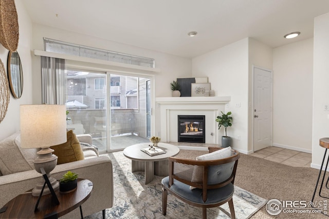 living area featuring light colored carpet, a glass covered fireplace, light tile patterned flooring, and baseboards