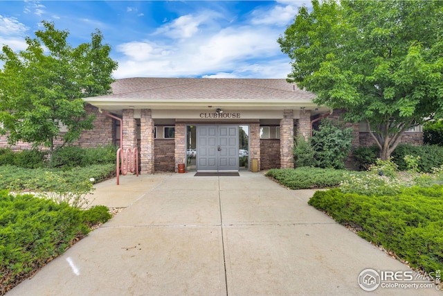 view of front of property featuring driveway, stone siding, a shingled roof, and a porch