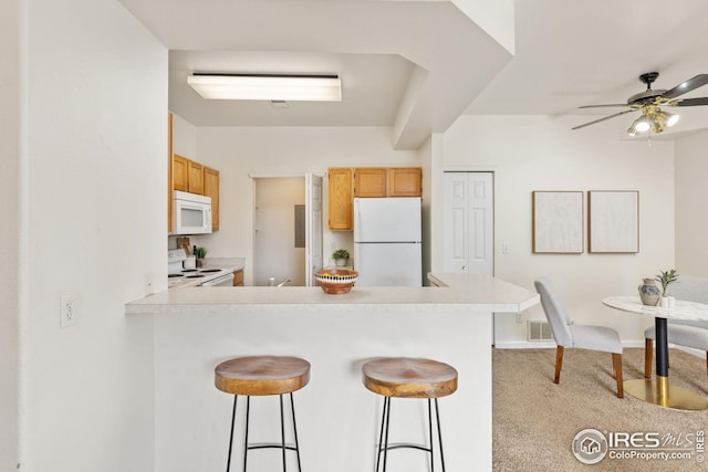kitchen featuring light carpet, light countertops, white appliances, and a kitchen breakfast bar