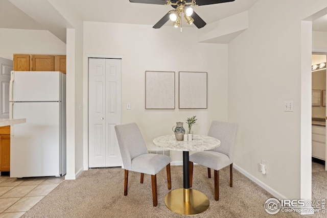dining room with light carpet, light tile patterned floors, ceiling fan, and baseboards