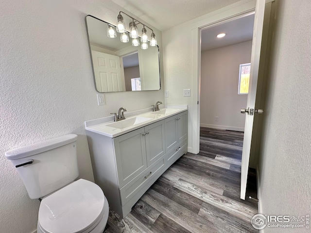 bathroom featuring double vanity, toilet, wood finished floors, and a sink