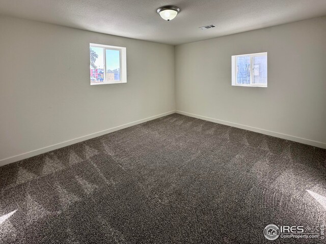 empty room featuring visible vents, dark carpet, a textured ceiling, and baseboards