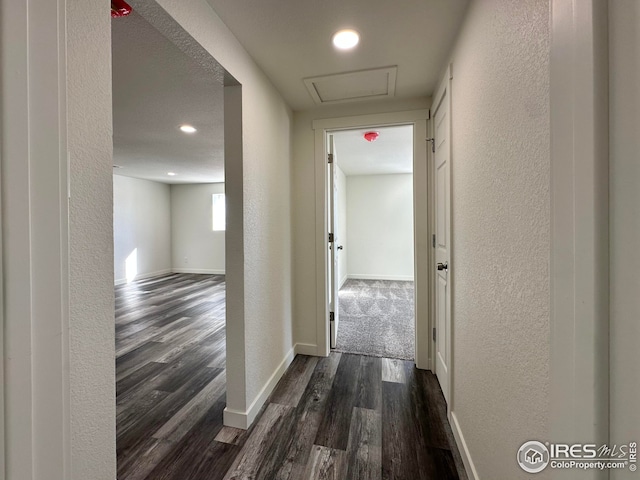 hall featuring dark wood finished floors, a textured wall, and baseboards