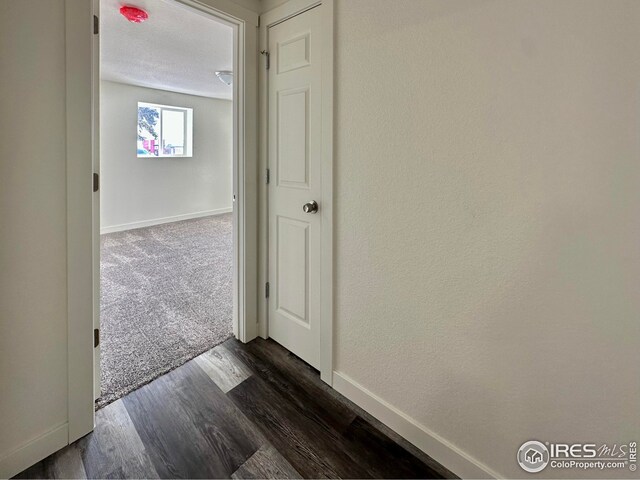 corridor featuring baseboards, dark wood-type flooring, dark carpet, and a textured ceiling
