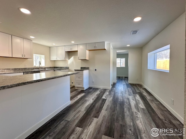kitchen with visible vents, a textured ceiling, dark countertops, dark wood finished floors, and white cabinets