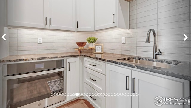 3806 Bridle Ridge Cir, Severance, CO 80524 - kitchen with white cabinetry, backsplash, dark stone counters, and stainless steel oven