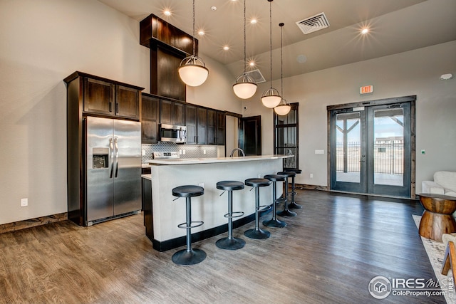 kitchen with a center island with sink, decorative light fixtures, dark brown cabinets, appliances with stainless steel finishes, and a breakfast bar area