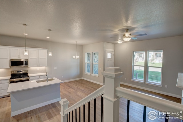 kitchen with light hardwood / wood-style flooring, stainless steel appliances, white cabinets, decorative light fixtures, and sink