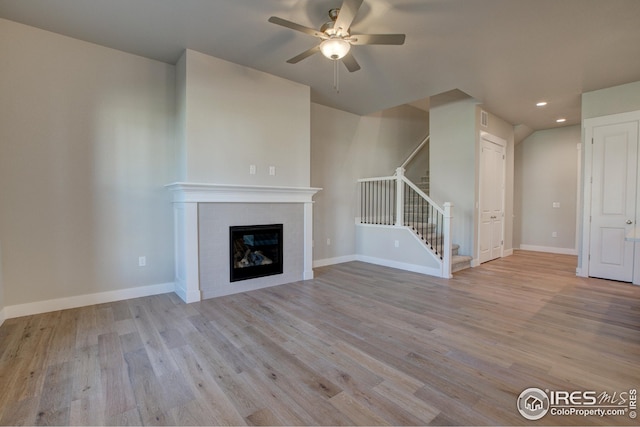 unfurnished living room with light wood-type flooring, a tiled fireplace, and ceiling fan