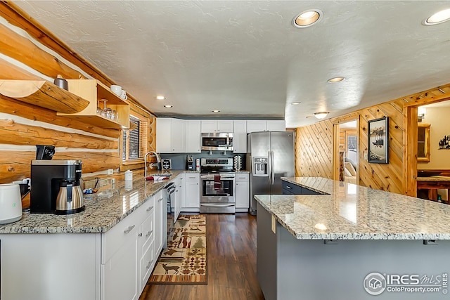 kitchen with appliances with stainless steel finishes, a sink, dark wood finished floors, white cabinetry, and light stone counters