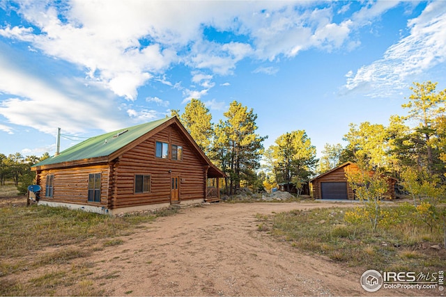 view of side of home featuring log siding, dirt driveway, a detached garage, and metal roof