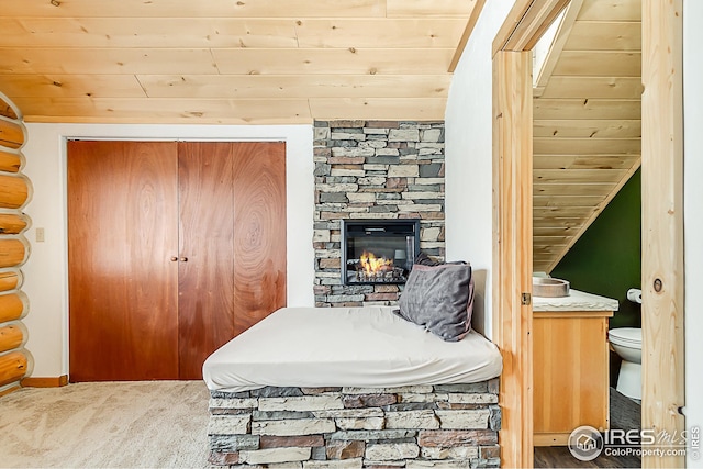 carpeted bedroom with wooden ceiling, a stone fireplace, and a closet