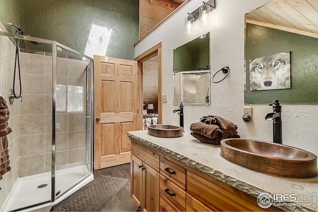 bathroom featuring a textured wall, a shower stall, double vanity, and wood finished floors