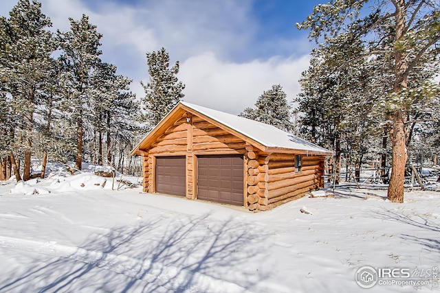 snow covered property featuring log siding, a garage, and an outdoor structure