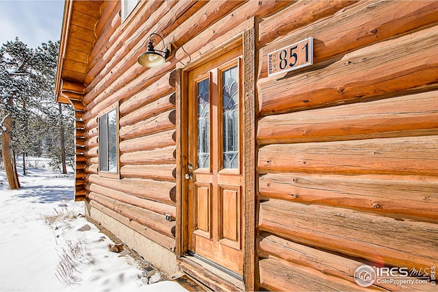 snow covered property entrance with log exterior