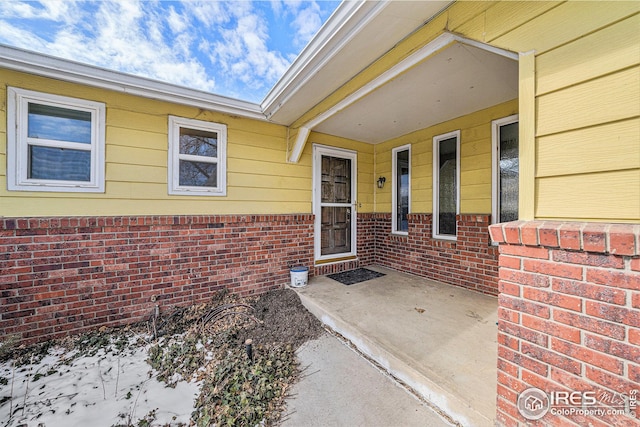 snow covered property entrance with a patio and brick siding