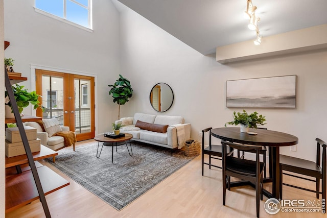 living room featuring a towering ceiling, light wood finished floors, and french doors