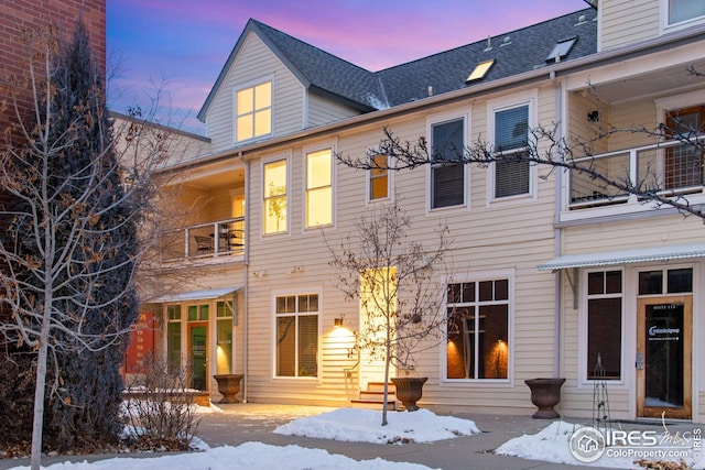 snow covered property featuring a shingled roof and a balcony