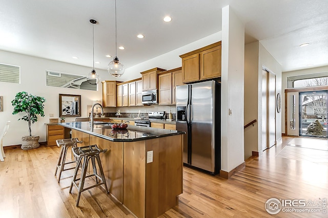 kitchen featuring dark countertops, a breakfast bar area, stainless steel appliances, decorative light fixtures, and brown cabinets