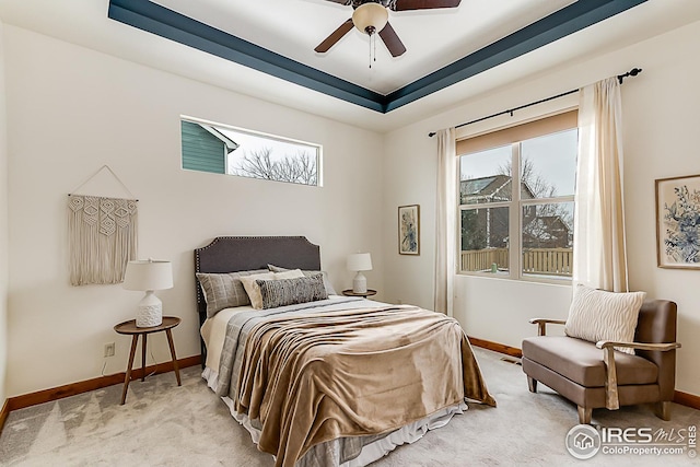 bedroom with baseboards, light colored carpet, and a raised ceiling