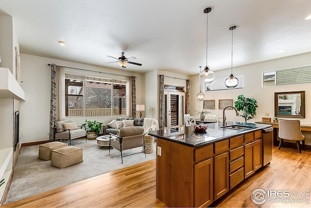 kitchen featuring a sink, dark countertops, decorative light fixtures, an island with sink, and brown cabinetry