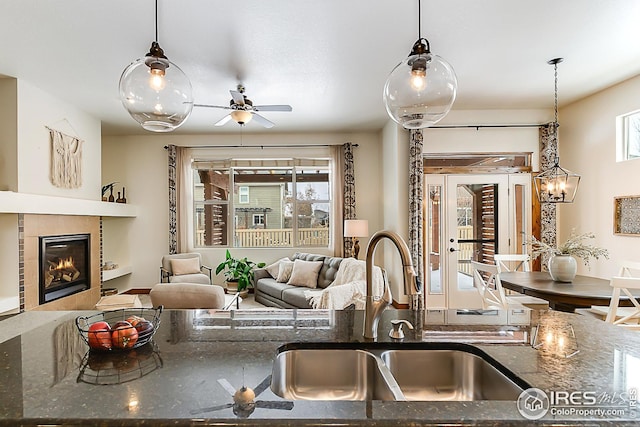 kitchen featuring hanging light fixtures, open floor plan, dark stone counters, and a sink