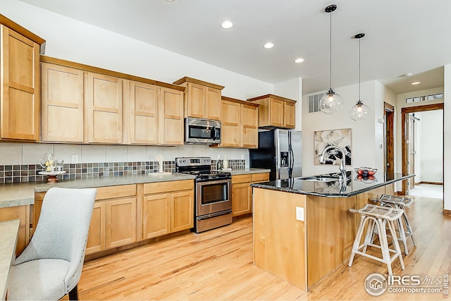 kitchen featuring a sink, dark countertops, pendant lighting, an island with sink, and stainless steel appliances