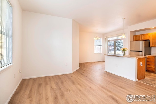 kitchen with brown cabinetry, freestanding refrigerator, hanging light fixtures, light countertops, and light wood-type flooring