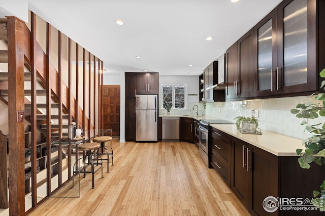 kitchen with a sink, stainless steel appliances, dark brown cabinetry, light countertops, and decorative backsplash