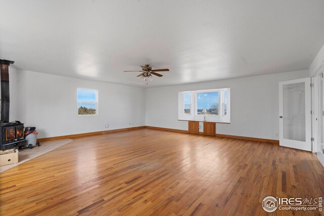 24525 County Road 53, Kersey, CO 80644 - unfurnished living room featuring ceiling fan, light wood-type flooring, a wood stove, and baseboards