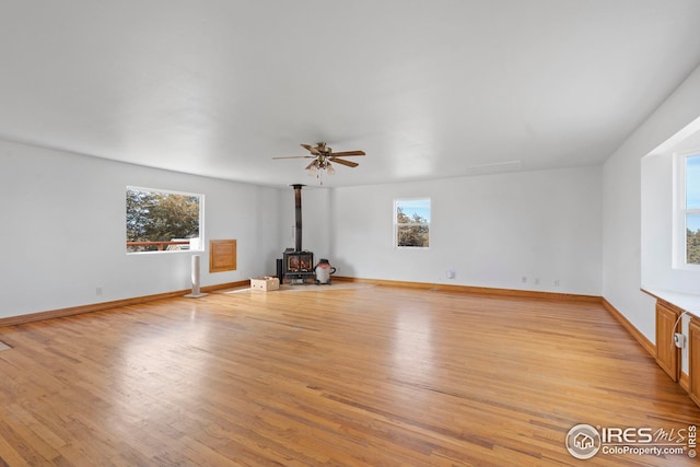 24525 County Road 53, Kersey, CO 80644 - unfurnished living room with baseboards, ceiling fan, a wood stove, and light wood-style floors