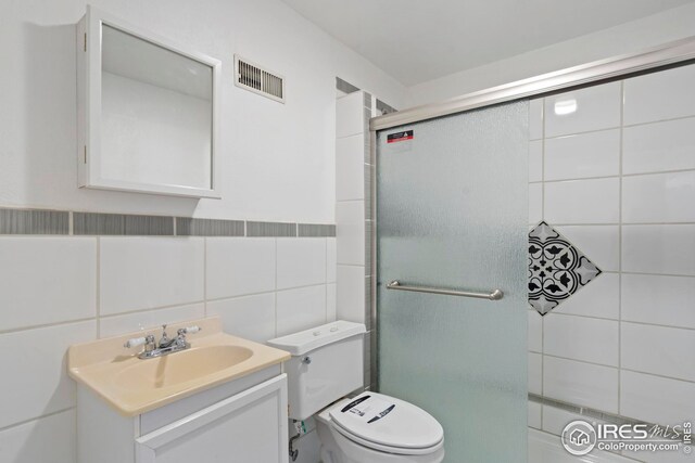 24525 County Road 53, Kersey, CO 80644 - bathroom featuring toilet, a shower with shower door, vanity, visible vents, and tile walls